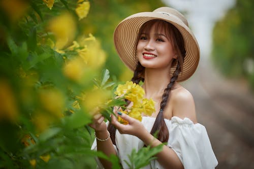 Beautiful Woman in White Off Shoulder Wearing Hat Holding Yellow Flowers 