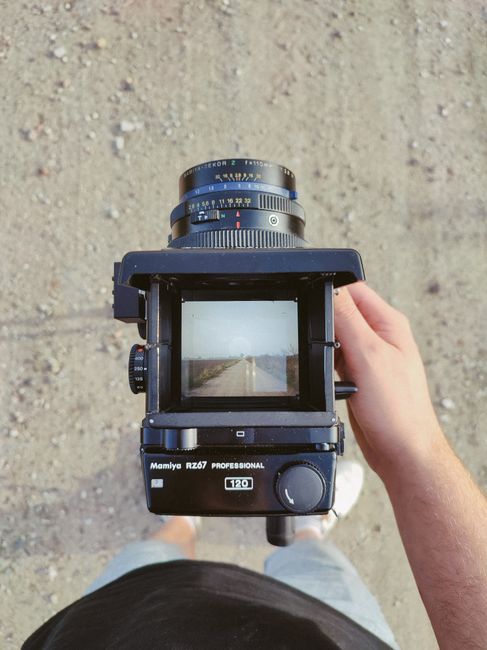 A person holding a vintage camera capturing a scenic road through the viewfinder outdoors.