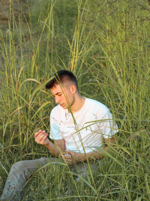 A Man Wearing a White Shirt Sitting on a Grass Field