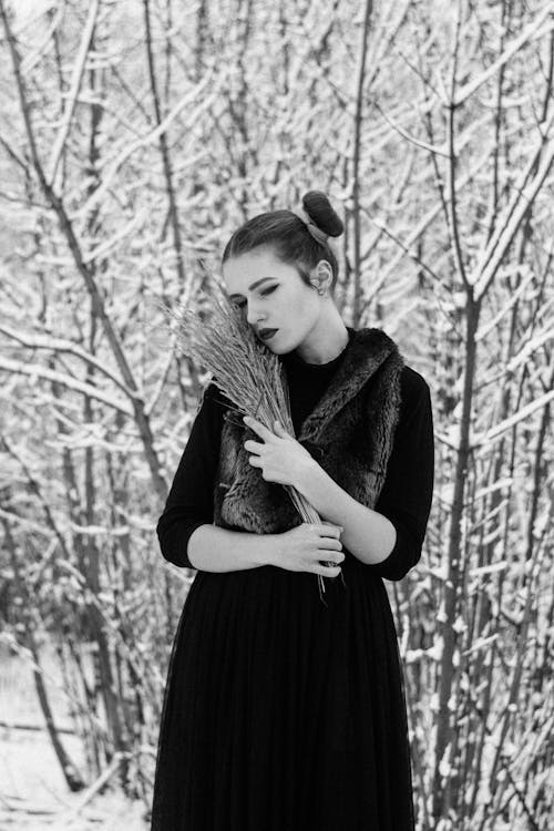 Free A Grayscale of a Woman Wearing a Black Outfit Holding Dried Reed Stock Photo