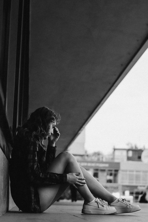 Free Black and white portrait of a young woman sitting outside, deep in thought. Stock Photo