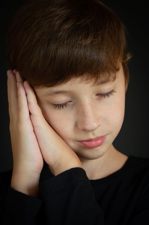 Free Close-up portrait of a young boy with eyes closed, hands together, appearing peaceful and serene. Stock Photo