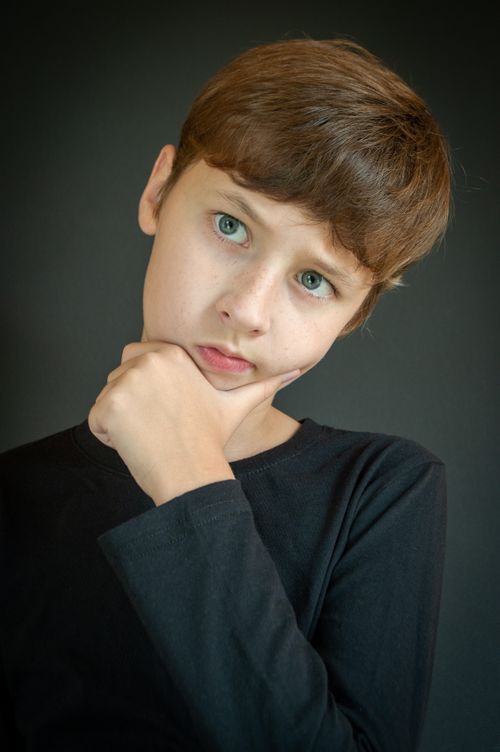 Free Portrait of a young boy in a black sweater, looking thoughtful against a dark background. Stock Photo