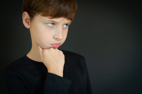 Free Thoughtful child with brown hair on a dark backdrop in studio setting. Stock Photo