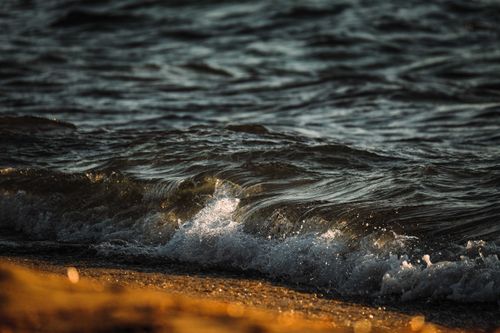 Free A close-up of waves gently crashing on a sandy beach during sunset, capturing the serene ocean ambiance. Stock Photo