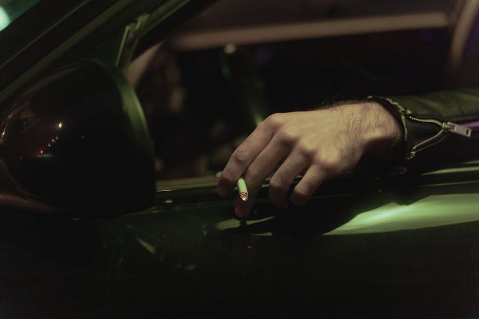 Helix Midnight vs WinkBed: Side Sleeper Back Pain A man with a leather jacket holds a cigarette out of a car window at night, creating a cool, moody setting.