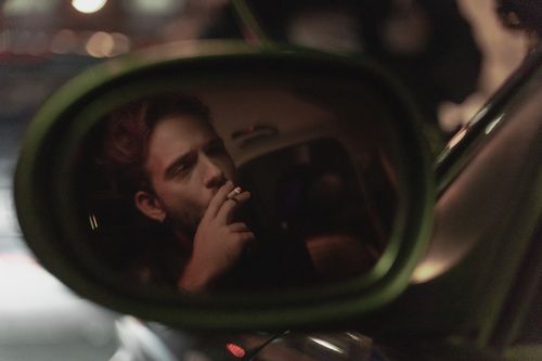 Free Reflection of a young man smoking in a car's side mirror during nighttime. Stock Photo