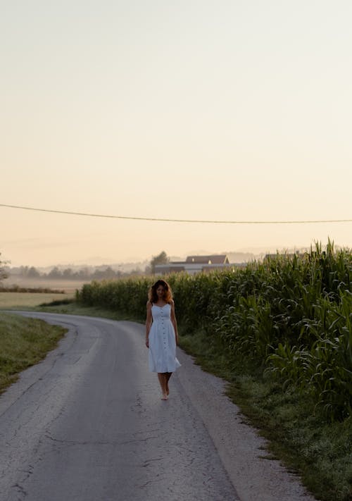 Free Woman in White Dress Walking Barefoot in a Country Road Stock Photo