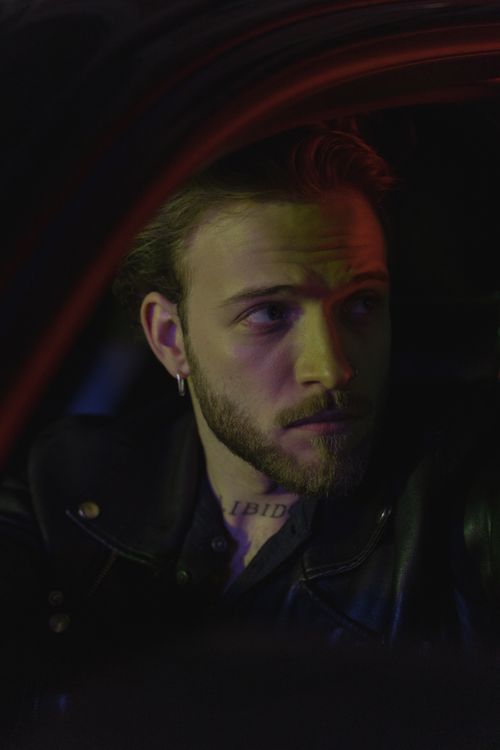 Free A bearded man in a leather jacket seated in a car at night, looking contemplative. Stock Photo