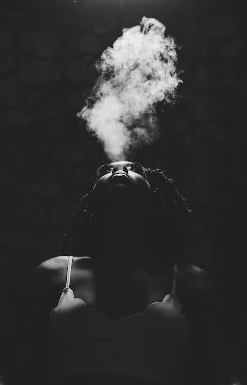 Grayscale Photo of a Person Blowing Out Smoke