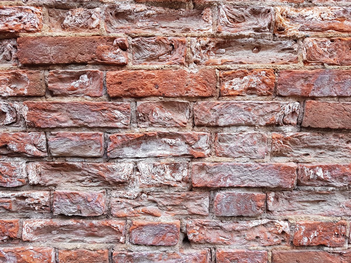 Aged brick wall with spalling faces and worn mortar in need of restoration