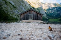 乡村小屋坐落于宁静的山间湖泊旁，四周环绕着郁郁葱葱的绿色植物和崎岖的悬崖