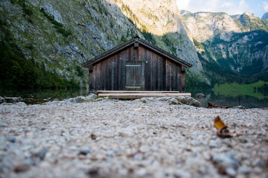 乡村小屋坐落于宁静的山间湖泊旁，四周环绕着郁郁葱葱的绿色植物和崎岖的悬崖