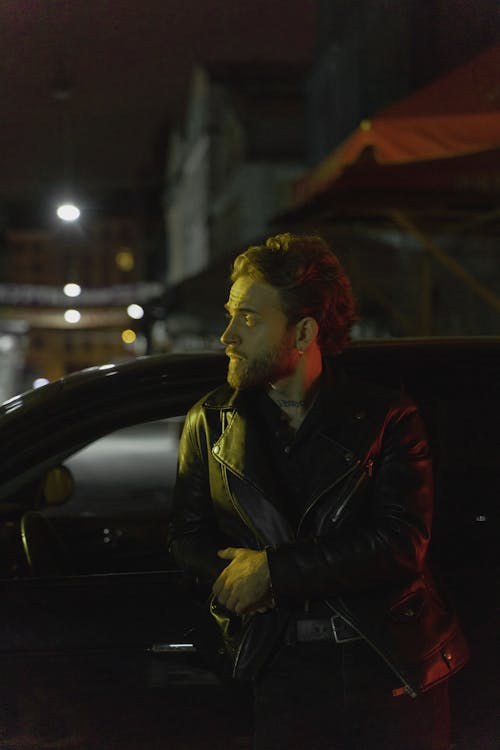 Man in Black Leather Jacket Leaning on Car during Night Time