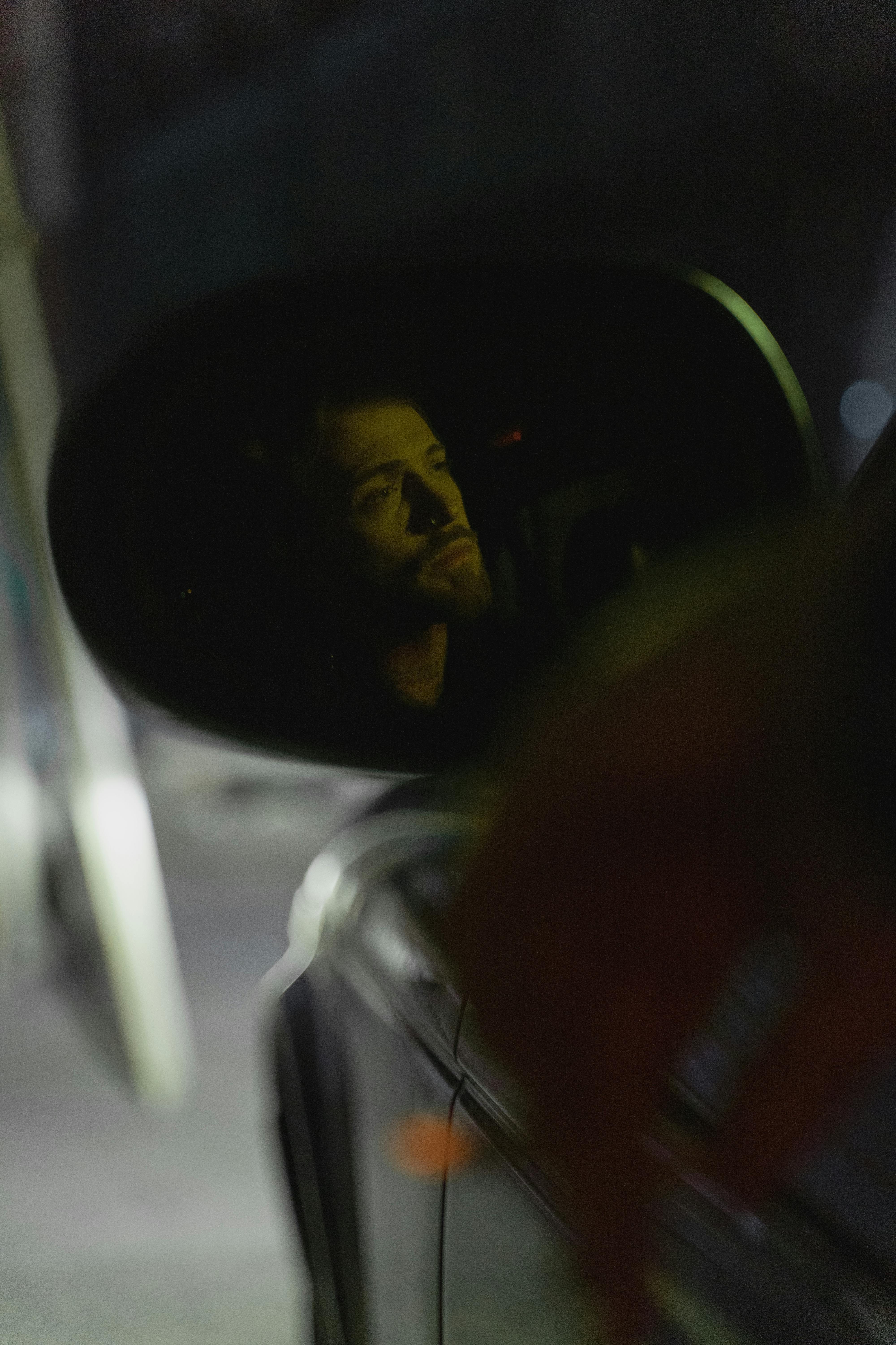 Nighttime car side mirror reflection captures a man's thoughtful gaze.