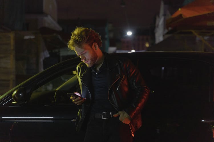 Man In Black Leather Jacket Standing Beside Black Car During Night Time