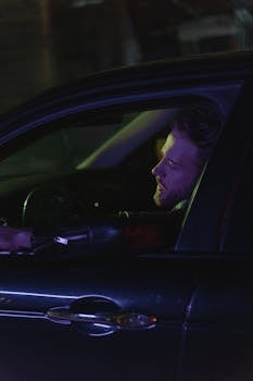 Caucasian man with a beard driving a car at night, exuding a cool retro vibe.