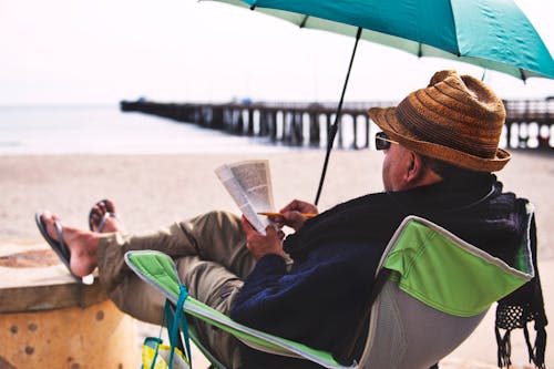 Man Sitting on Chair Under Blue Umbrella Near Beach