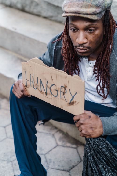 Free A man sitting on outdoor steps holding a sign that reads 'Hungry'. Stock Photo