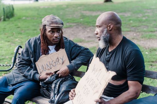 Free Two men sitting on a bench in a park holding signs about hunger and work. Stock Photo