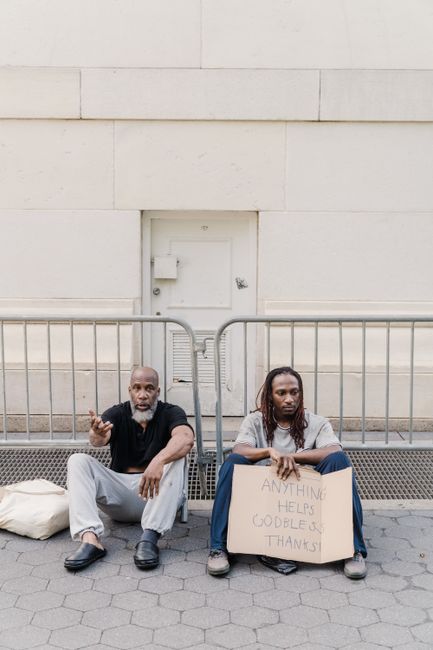 Two homeless men sitting on city sidewalk holding a sign seeking help. Two homeless men sitting on city sidewalk holding a sign seeking help.