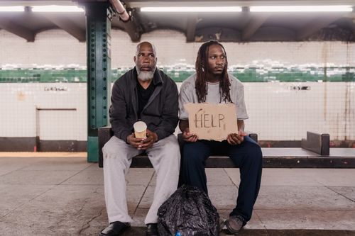 Free Two men in a subway station holding a help sign, highlighting financial hardship and homelessness. Stock Photo