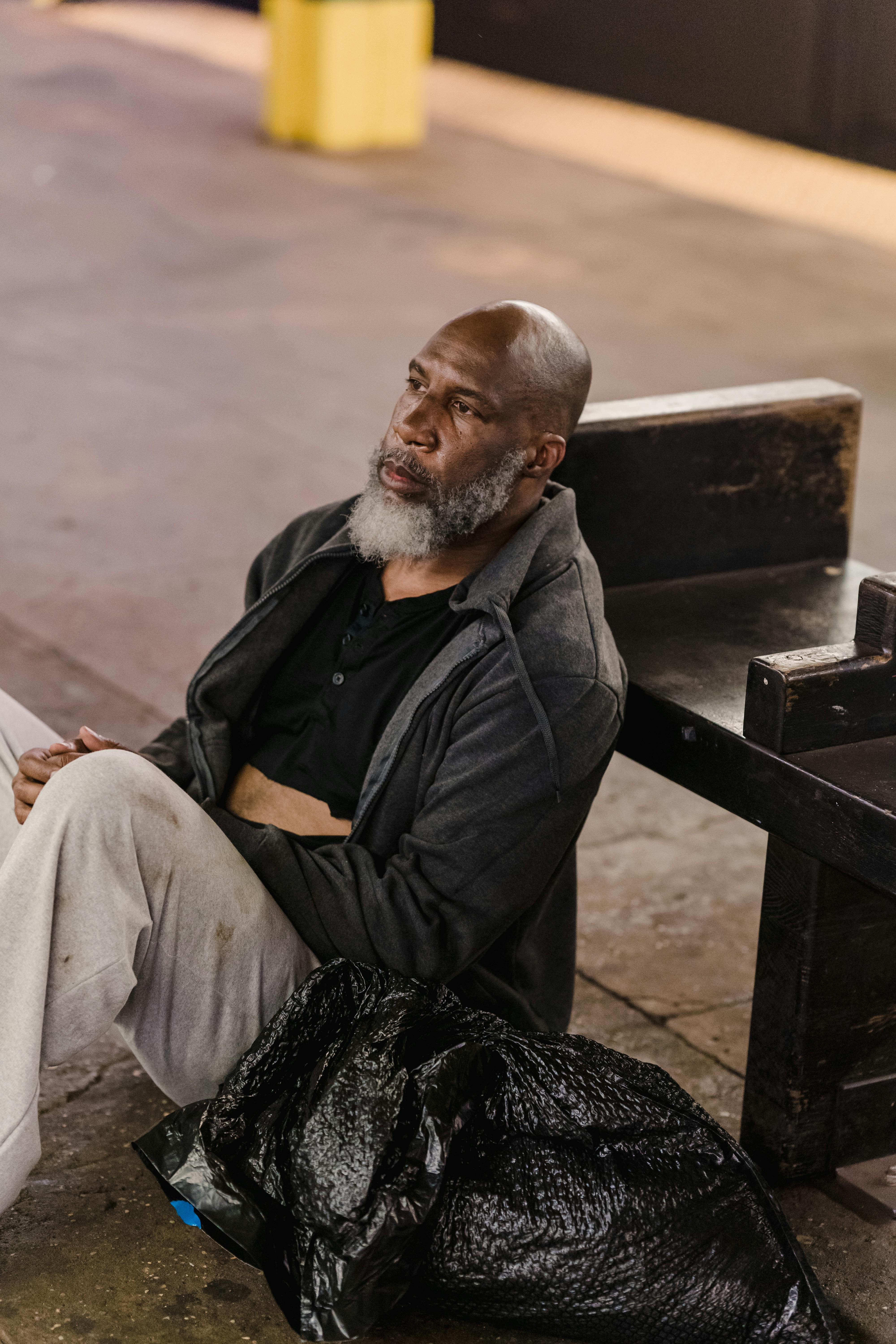 man in black jacket sitting on brown wooden bench