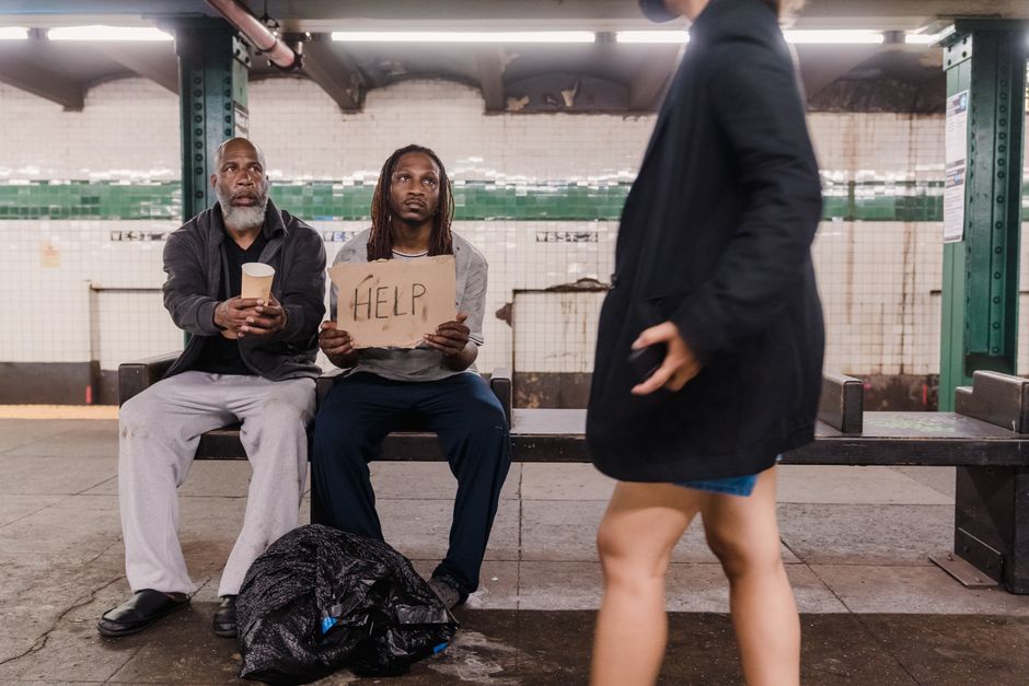 Dos hombres buscando ayuda en una plataforma de metro, destacando la pobreza urbana y problemas sociales.