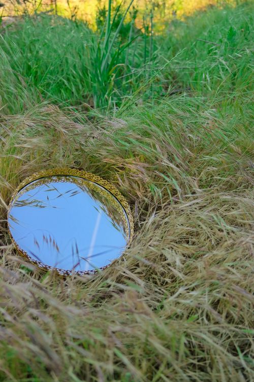 Free A round mirror reflects the sky, surrounded by lush, green grass. Stock Photo