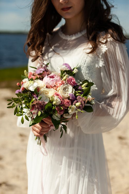 Woman in White Wedding Dress Holding Bouquet of Flowers