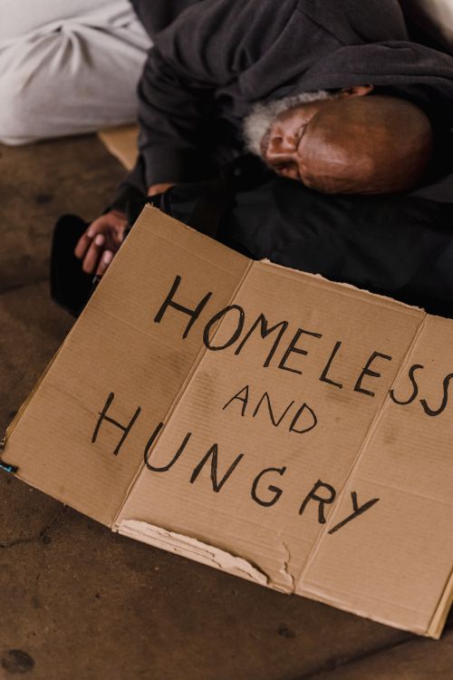 Free African American man resting on street with cardboard sign reading 'Homeless and Hungry'. Stock Photo