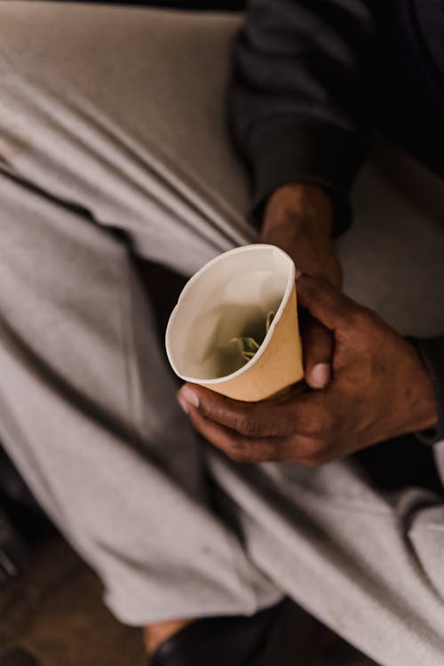 A Homeless Person Holding a Cup with Money