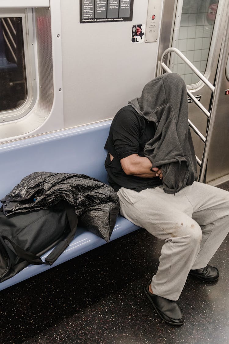 Man In Black Shirt And Beige Pants Sleeping Inside A Train With Face Covered