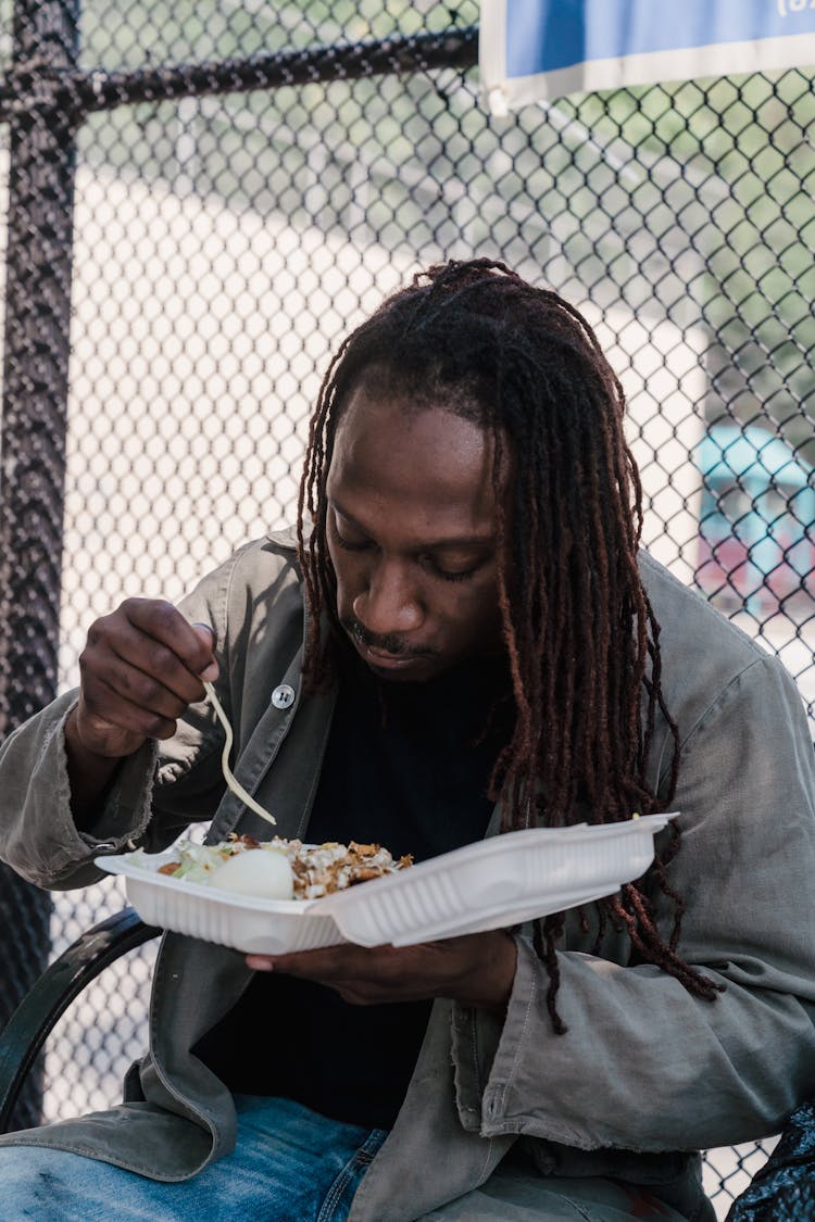 A Man Eating Food In A Disposable Container