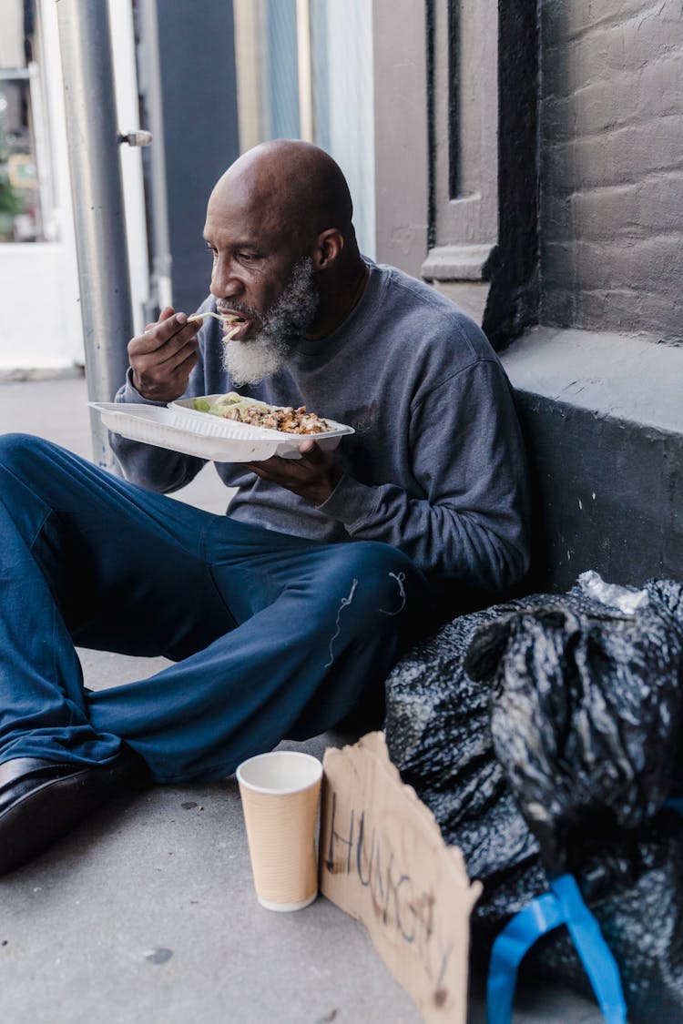 Homeless Man Eating While Sitting On Floor 