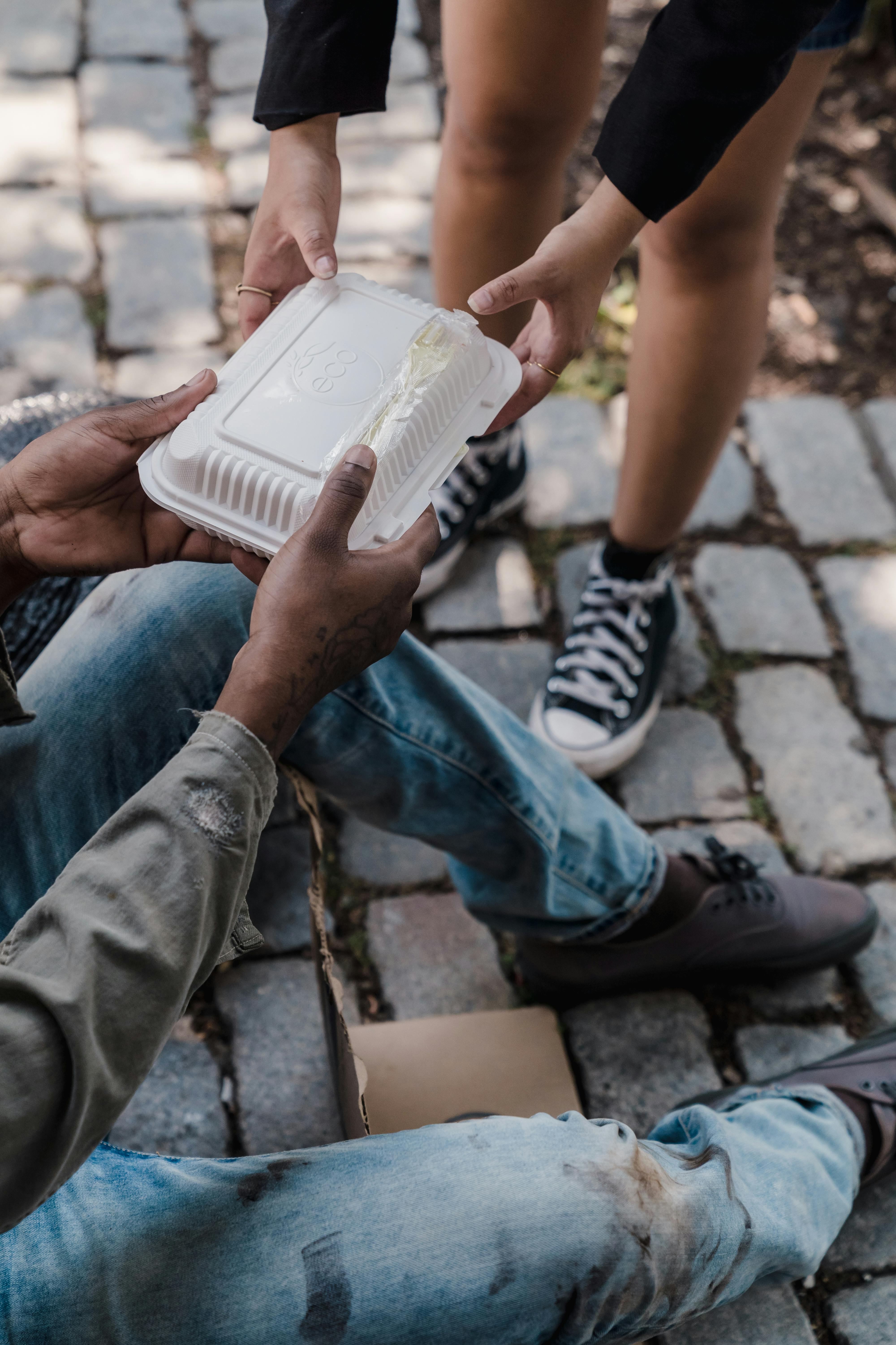 a person handing out food to a person in shabby clothes