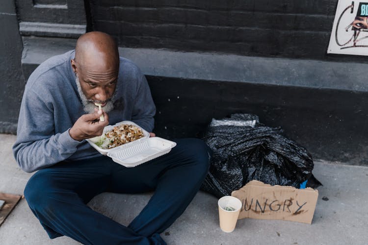 Homeless Man Eating On Sidewalk