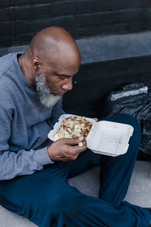 Free A man sitting on outdoor steps eating a takeaway meal from a container. Stock Photo