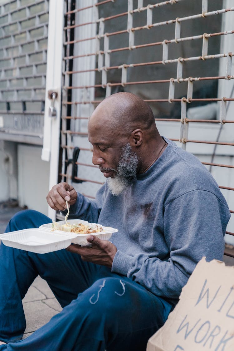 Man Sitting On Sidewalk And Eating A Takeway Meal