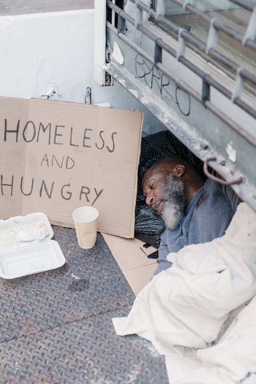 A Man Sleeping on the Street with a Placard Homeless and Hungry
