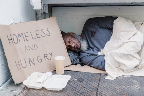 Free Photo of a Homeless Man Sleeping Near a Cardboard Sign Stock Photo