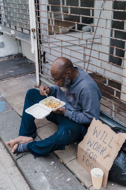 Free An African American homeless man eating food on the sidewalk with a cardboard sign. Stock Photo