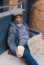 Homeless Man in Black Jacket Holding Paper Cup