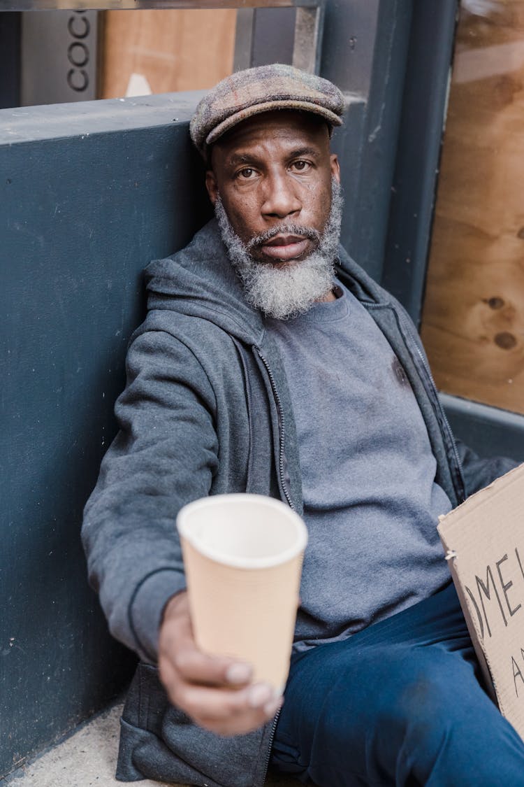 Homeless Man Holding A Paper Cup Asking For Help