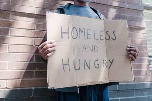 Free A close-up of a person holding a cardboard sign saying 'Homeless and Hungry' against a brick wall. Stock Photo