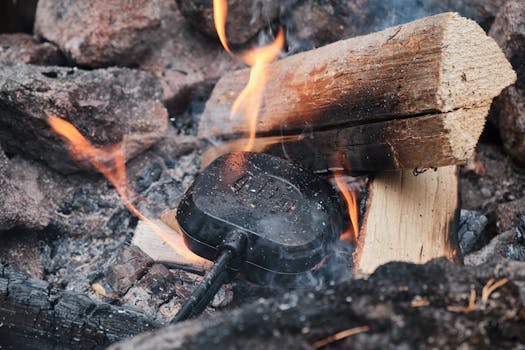 Campfire with burning logs and cooking gear in use, close-up view.