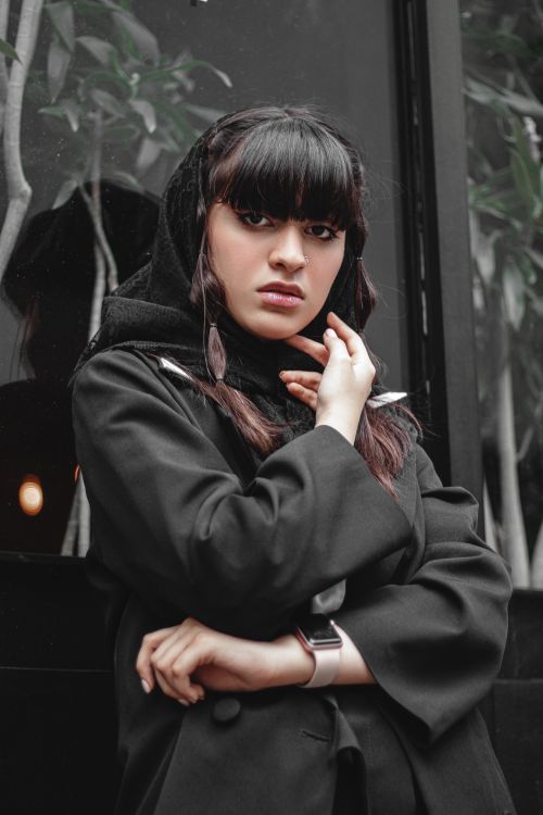 Free Stylish woman in black coat posing thoughtfully with hand on chin indoors. Stock Photo