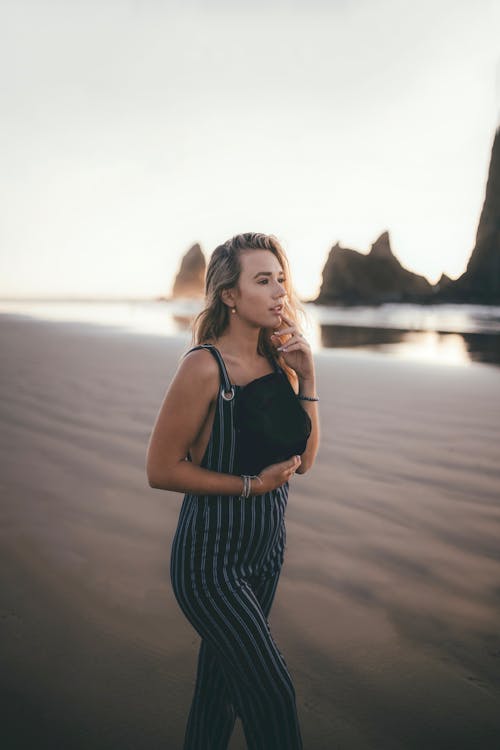 Free Woman in Black and White Stripe Tank Top Standing on Beach Stock Photo