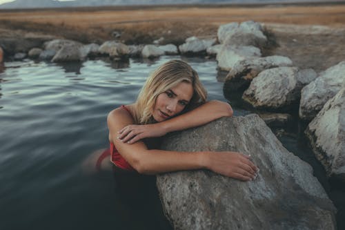 Woman in Red Bikini Sitting on Rock Near Body of Water