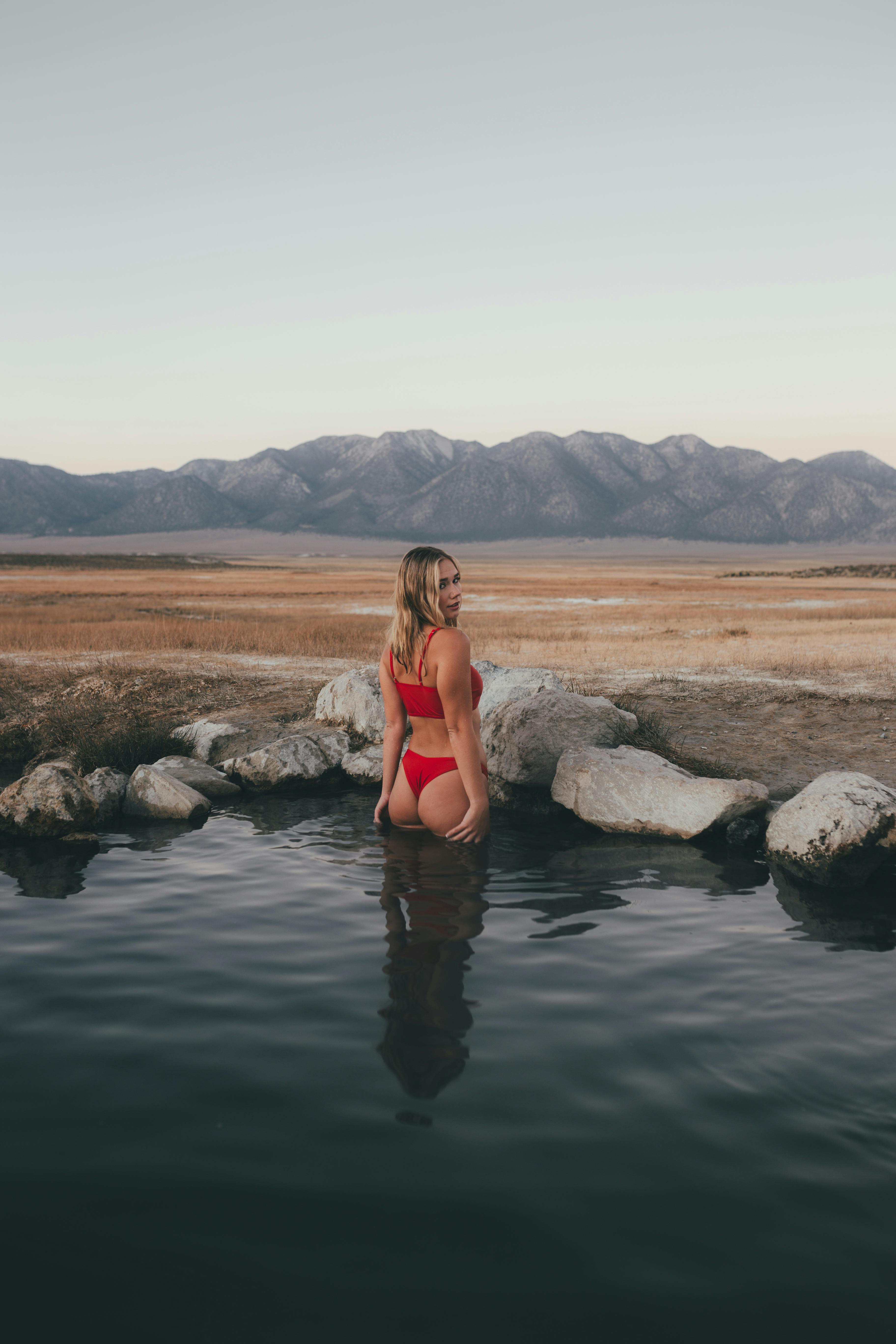 woman in red bikini sitting on rock in the middle of lake